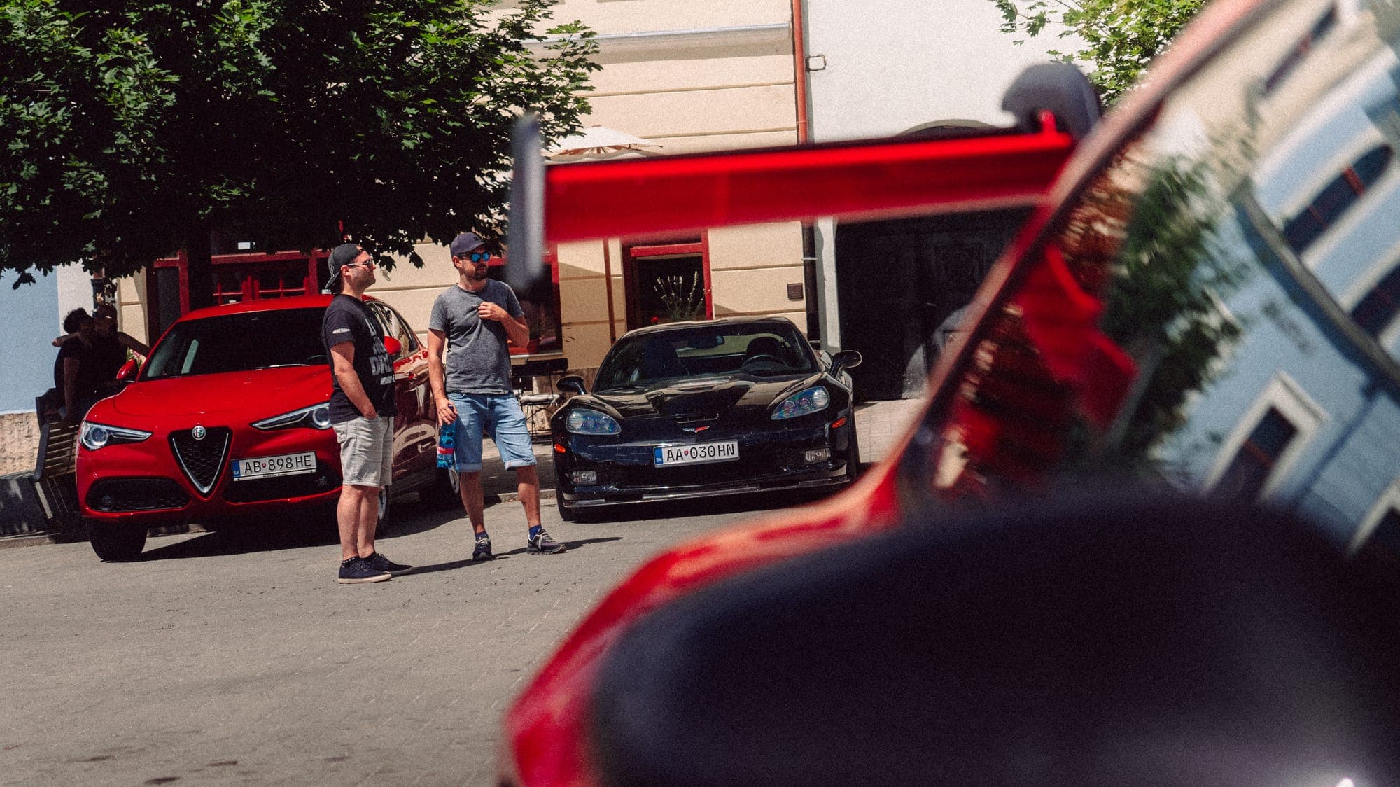 Účastníci pri autách na námestí, v popredí červené auto