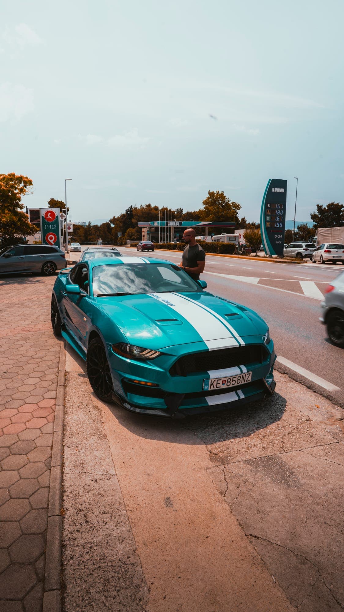 Tyrkysový Mustang s bielymi pruhmi na parkovisku