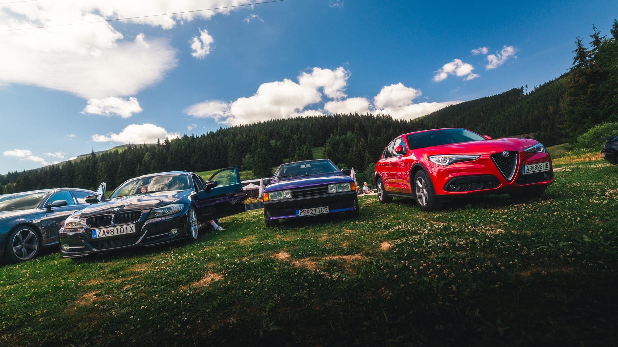 Autá na lúke, vpravo červená Alfa Romeo