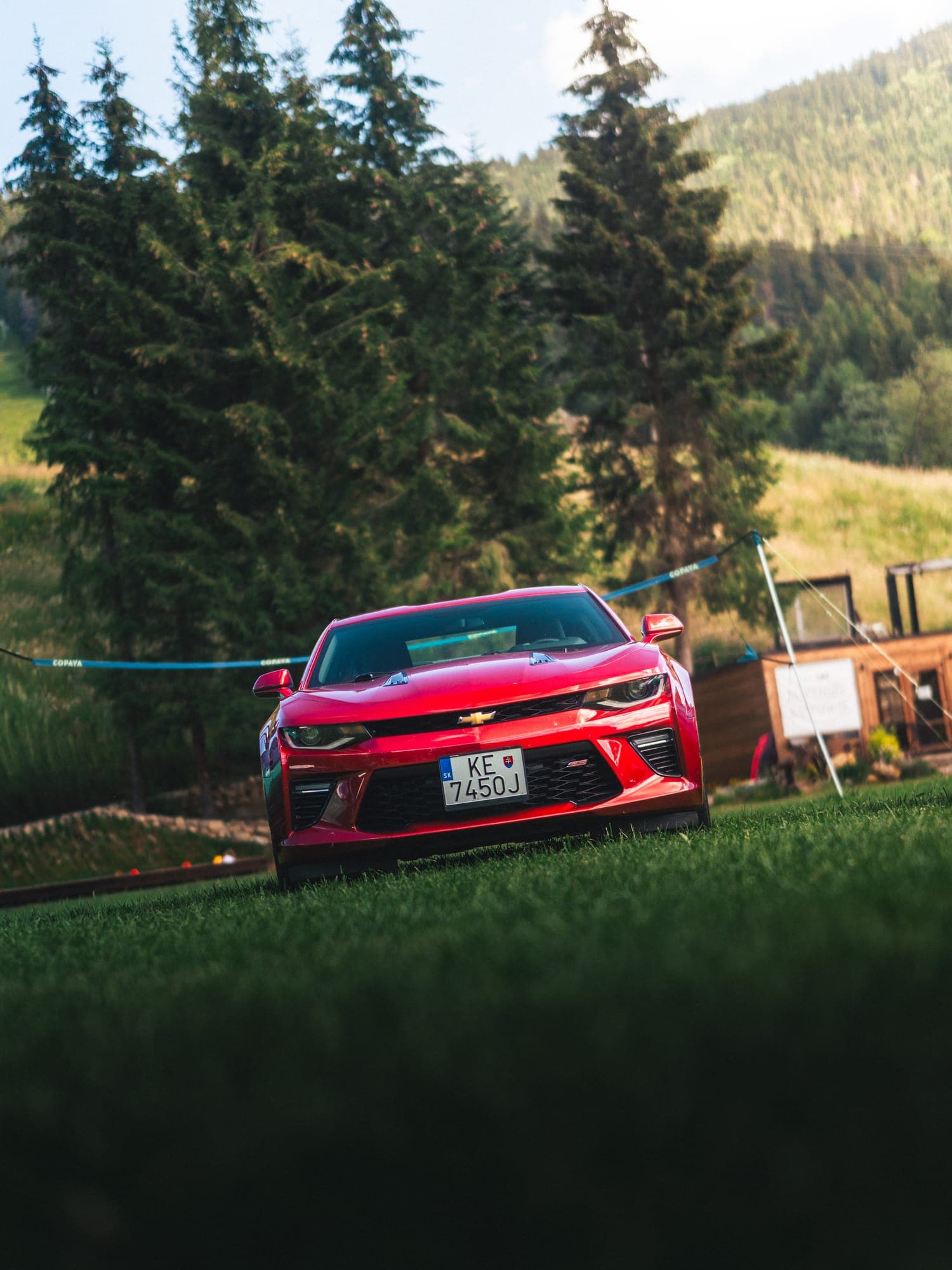 Červený Chevrolet Camaro pod smrekmi