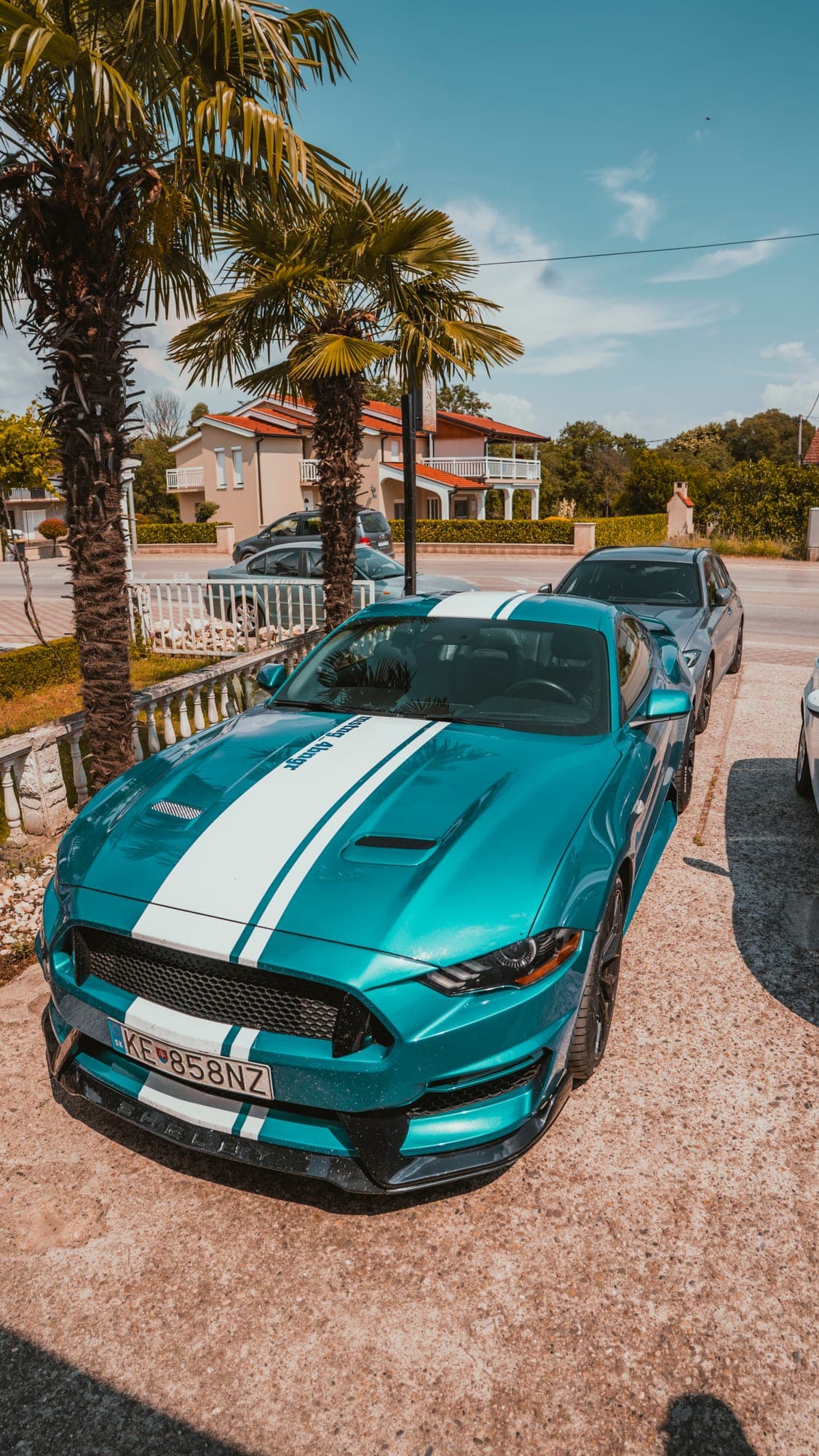Tyrkysový Mustang s bielymi pruhmi pod palmami