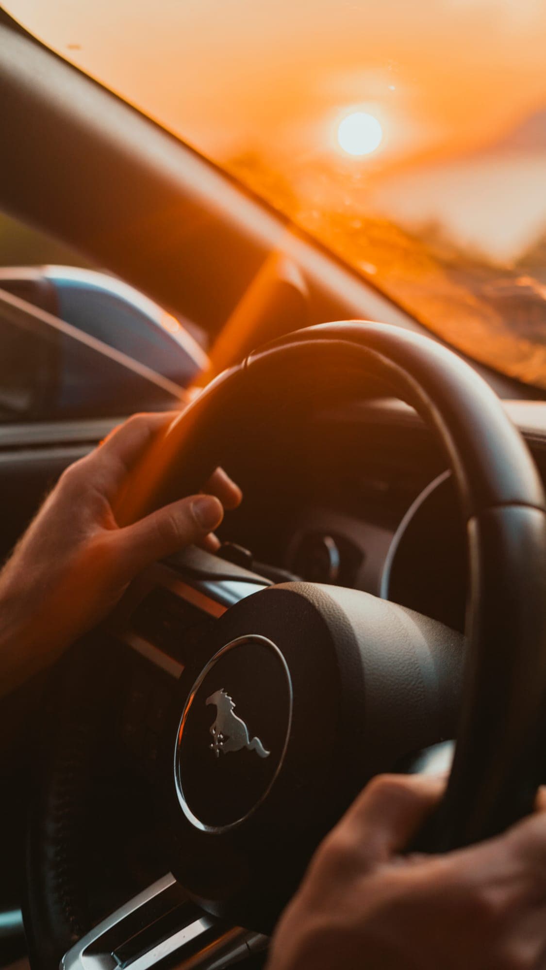 Ruky na volante Mustangu v zapadajúcom slnku